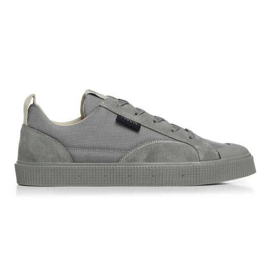 A side view of a Sanjo TESTE low-top sneaker featuring a sleek design with a grey Cordura nylon upper for durability and water resistance. Accented with suede overlays on the heel and toe for added texture. Includes a pull tab on the heel for easy wear and a tonal rubber outsole with textured detailing for grip. Finished with a subtle logo on the tongue and a contrasting purple inner lining.