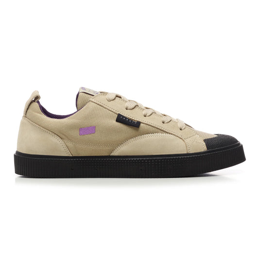 A side view of a Sanjo TESTE x Surge low-top sneaker, a limited-edition collaboration with Surge magazine. Features a taupe suede and Cordura nylon upper, purple embroidered logo details, a black rubber toe cap, and a textured black outsole for skate durability. Includes a Cordura tag highlighting the material's strength and water resistance.