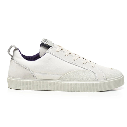 A side view of a Sanjo TESTE low-top sneaker featuring a sleek design with a white Cordura nylon upper for durability and water resistance. Accented with suede overlays on the heel and toe for added texture. Includes a pull tab on the heel for easy wear and a tonal rubber outsole with textured detailing for grip. Finished with a subtle logo on the tongue and a contrasting purple inner lining.