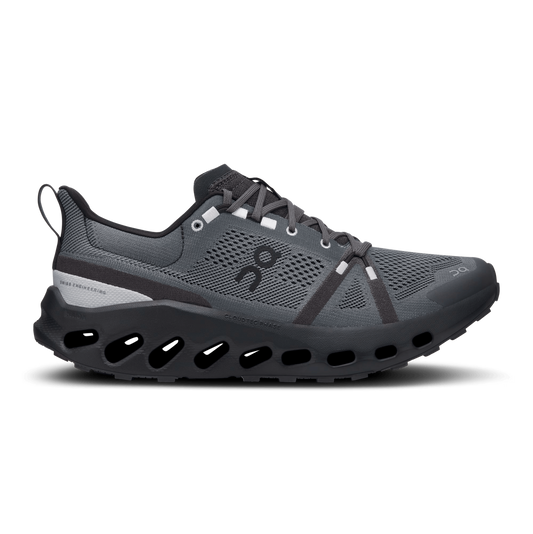 A side view of a dark gray On Running sneaker with black and silver accents, featuring a sleek design and a black perforated sole for cushioning and performance.